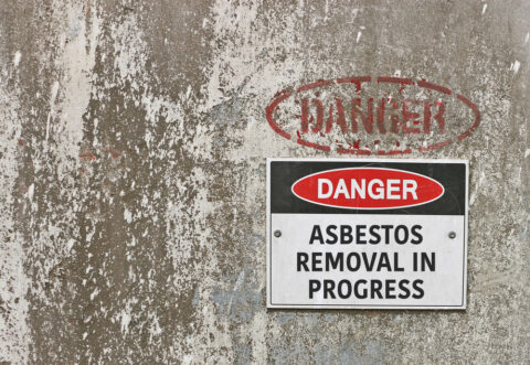 How to identify and treat asbestos in the workplace environment - asbestos surface with a visible warning sign attached.