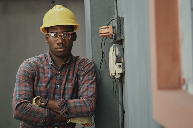 Strategies for promoting workplace mental health - construction worker with yellow hard hat standing arms crossed next to electrical connection.