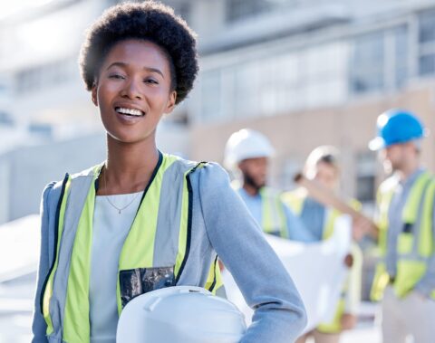 Smiling female professional in a safety vest and hard hat at a construction site, promoting workplace safety and gender representation in industries