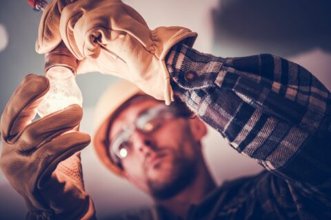Worker wearing protective gloves and safety gear installs a light bulb, emphasizing the importance of occupational hygiene in maintaining workplace safety