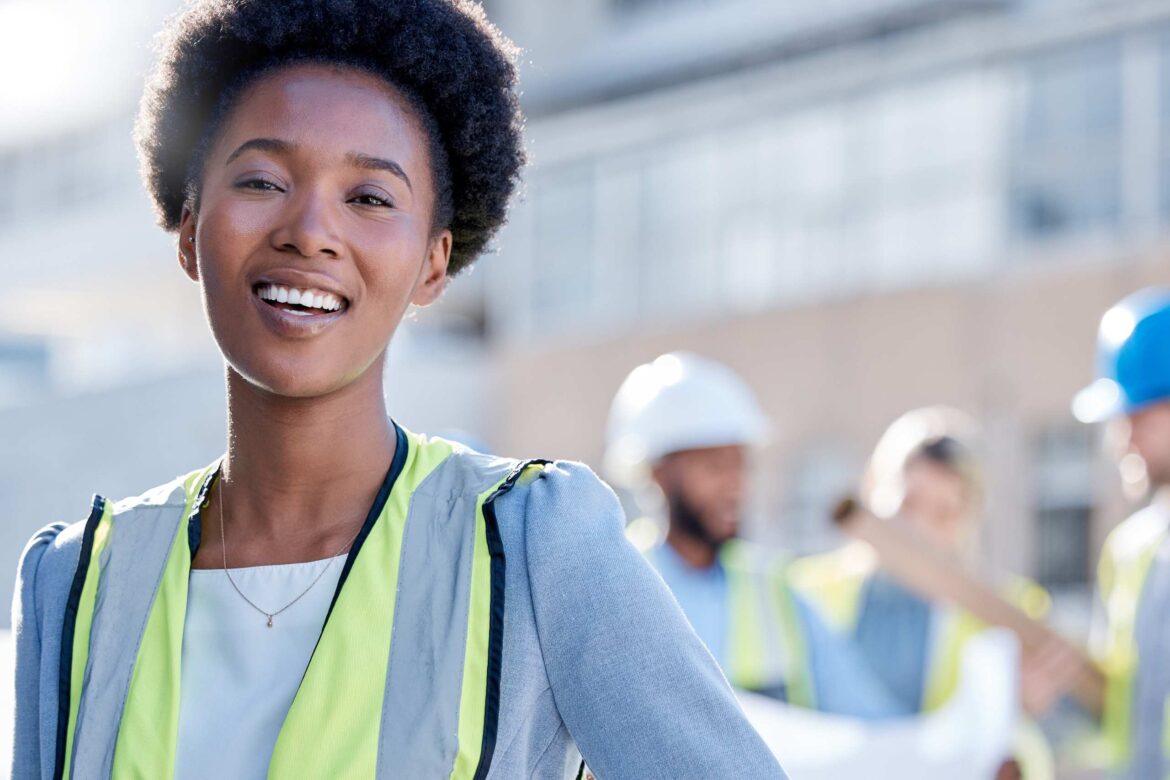 Smiling female professional in a safety vest and hard hat at a construction site, promoting workplace safety and gender representation in industries