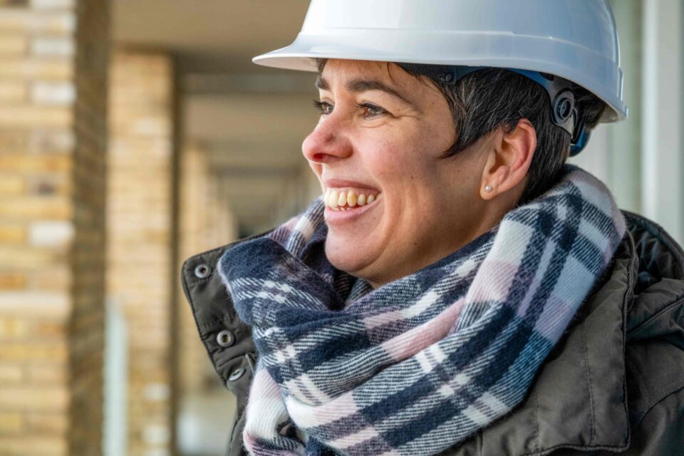 A smiling worker wearing a hard hat and scarf highlights the importance of ventilation assessment in preparing workplaces for cold stress during winter.