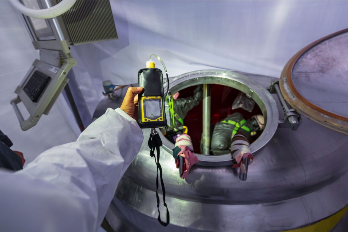 Technician performing an emissions test in an industrial tank to monitor air quality and ensure safety compliance in a controlled environment.