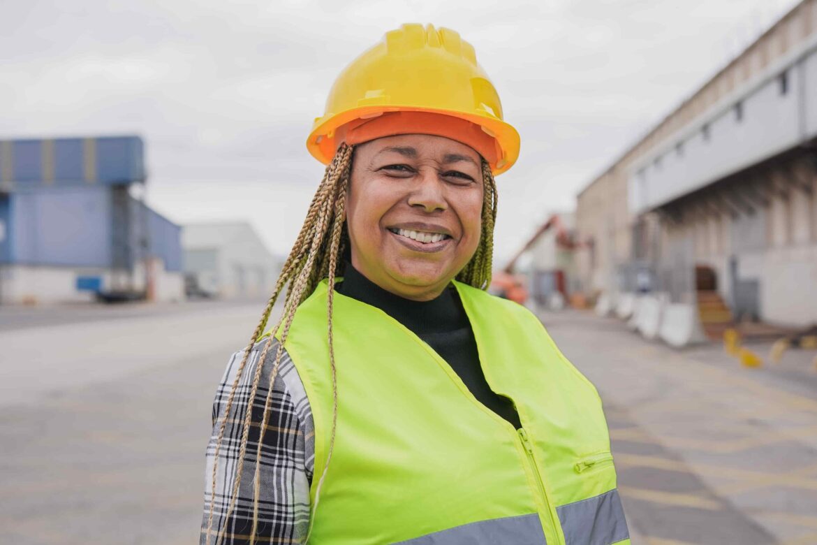 Smiling woman in safety gear at an industrial site, representing women's workplace health and safety in construction or manufacturing environments
