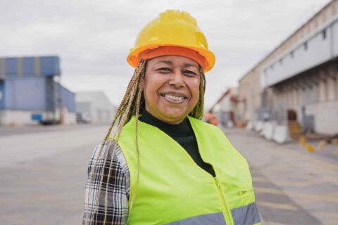 Smiling woman in safety gear at an industrial site, representing women's workplace health and safety in construction or manufacturing environments