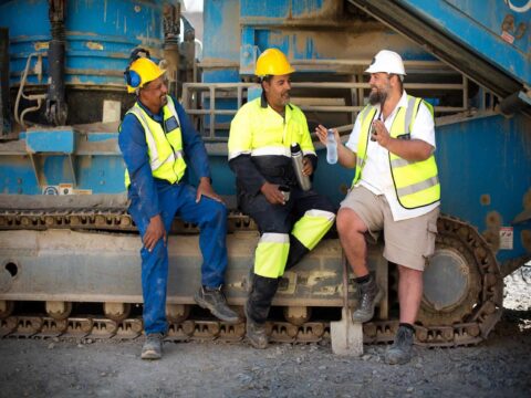 Industrial workers standing together in a warehouse, highlighting the importance of Men’s Health in the Workplace through safety and wellbeing practices.