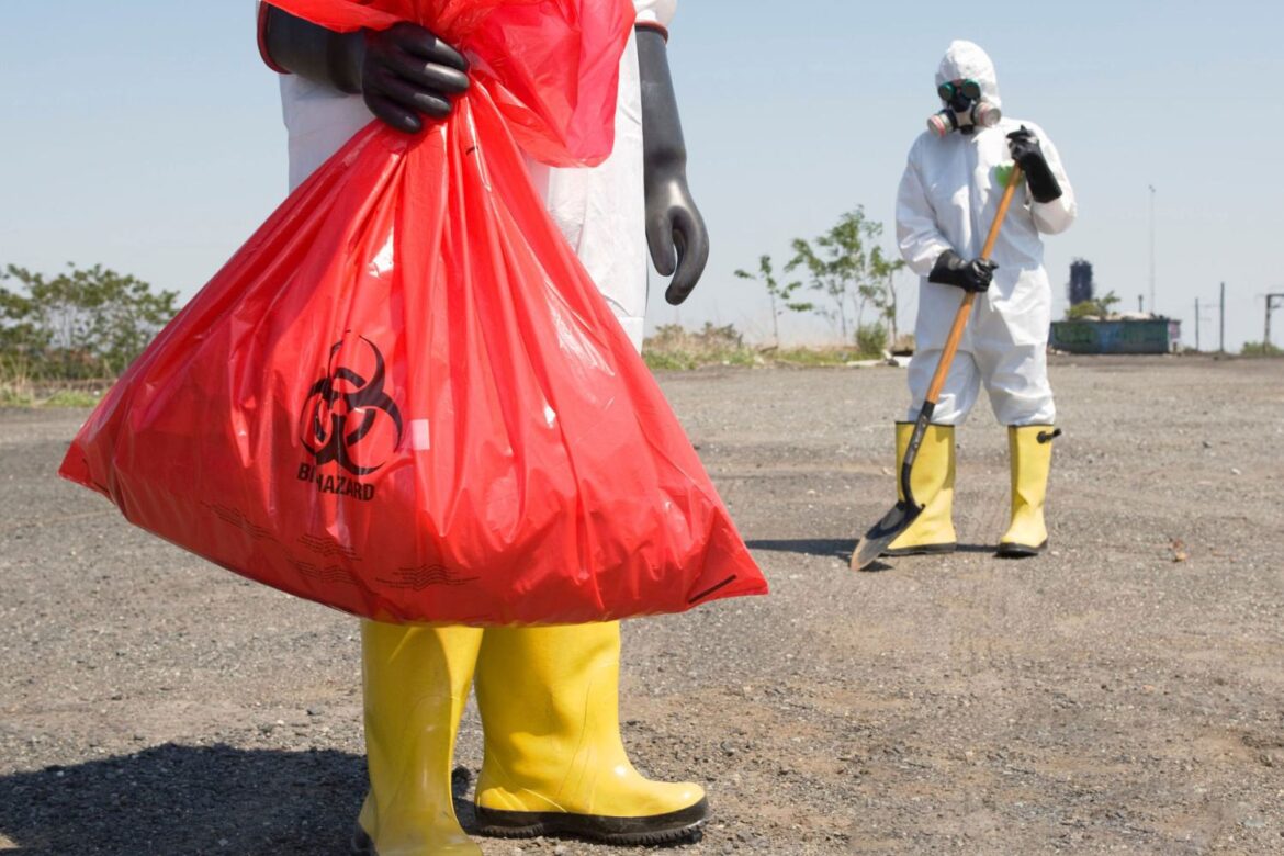 Workers in full PPE handling hazardous biological waste in red biohazard bags during site clean-up, representing safe disposal of Hazardous Biological Agents