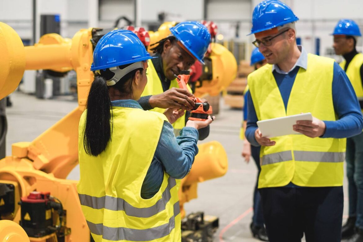 Workers wearing safety helmets and reflective vests participating in a health and safety training session inside an industrial facility, focusing on machinery operation and teamwork.