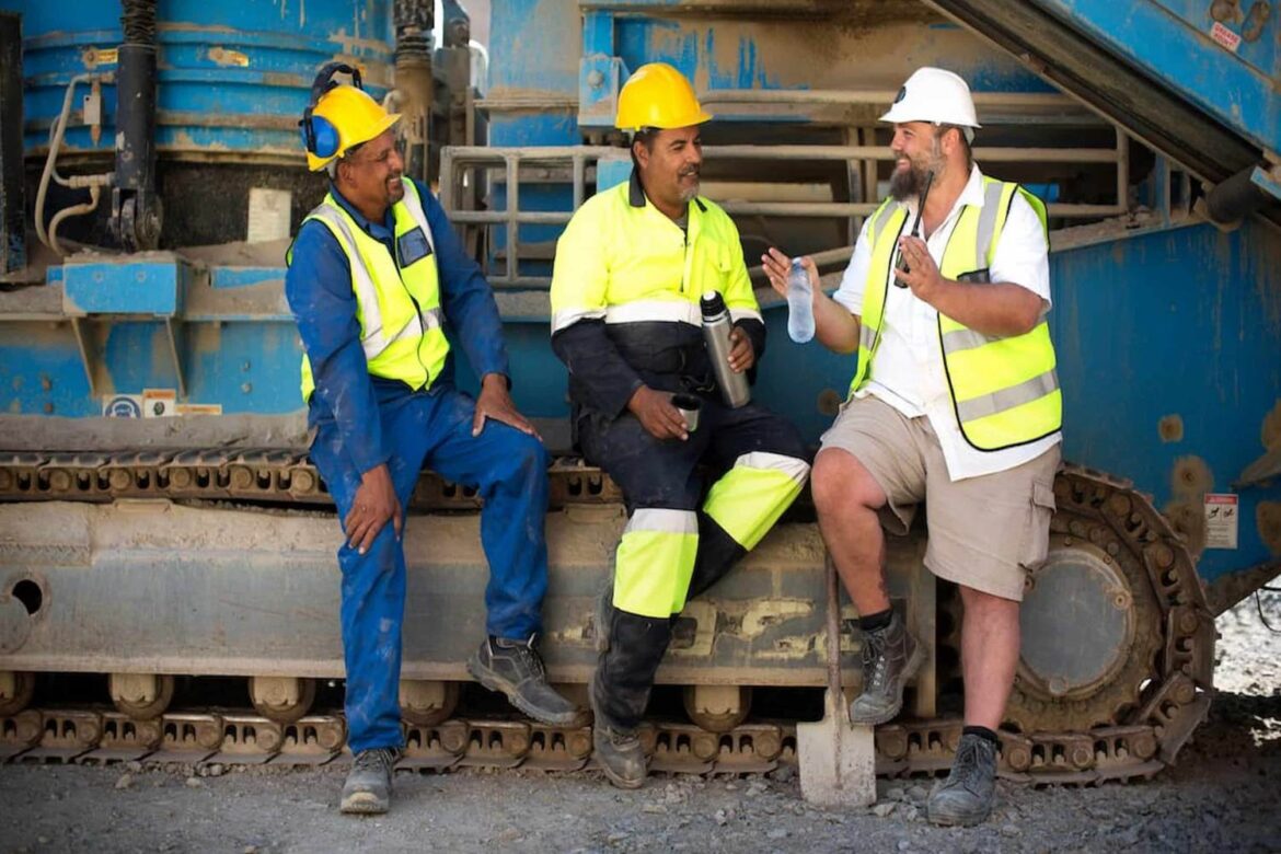 Industrial workers standing together in a warehouse, highlighting the importance of Men’s Health in the Workplace through safety and wellbeing practices.