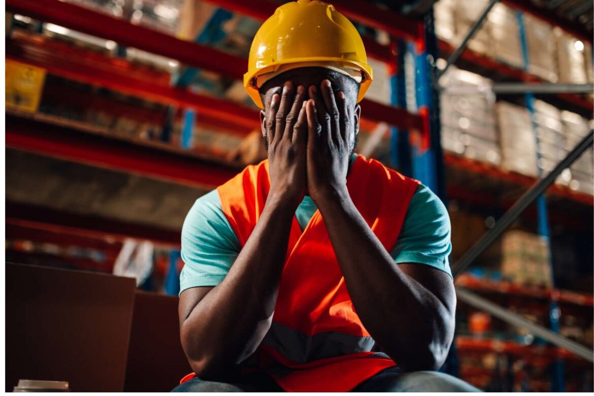 Worker experiencing workplace stress in an industrial warehouse environment highlighting the importance of environmental regulations for workplaces