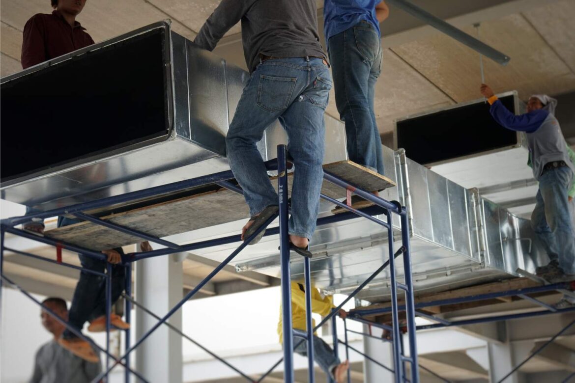 Workplace ventilation system installation with technicians fitting industrial air ducts to improve indoor air quality